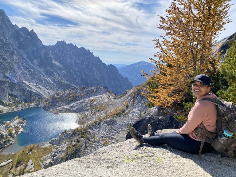 Rachel sits on a slab of granite overlooking a glaciated valley with larches.
