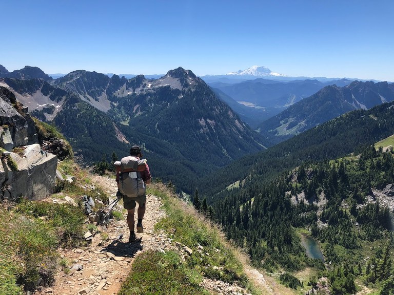 A hiker treks along PCT section J with Mount Rainier in the distance.