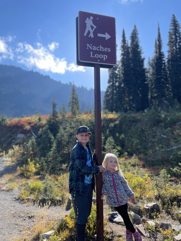 Two kids stand near a trail sign for Naches Loop. 