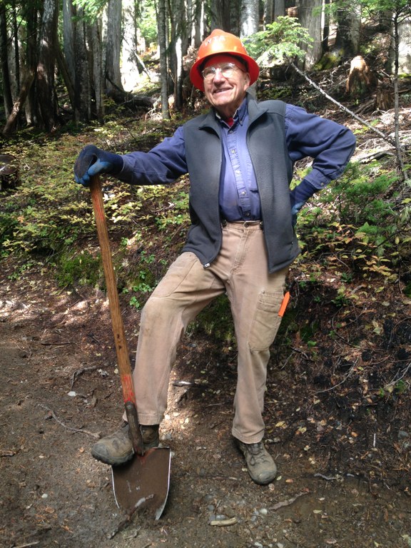 A volunteer stands with one foot on a shovel and looks proudly up at the sky.