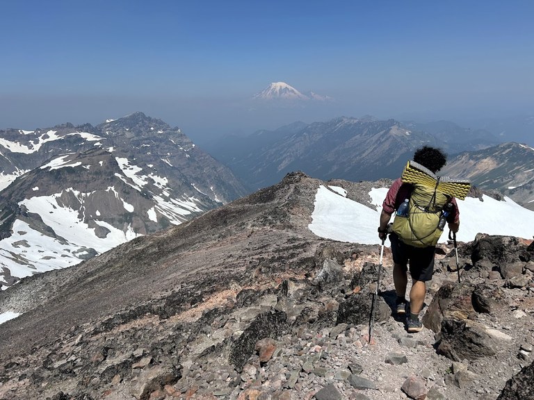 A hiker descends Old Snowy with Mount Rainier in the distance.