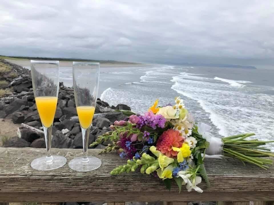 Enjoy your treats and decor, and then pack it out! Photo by Ashton Weis. Two flutes with drinks and a bouquet of flowers with the coast behind them. Photo by Ashton Weis.