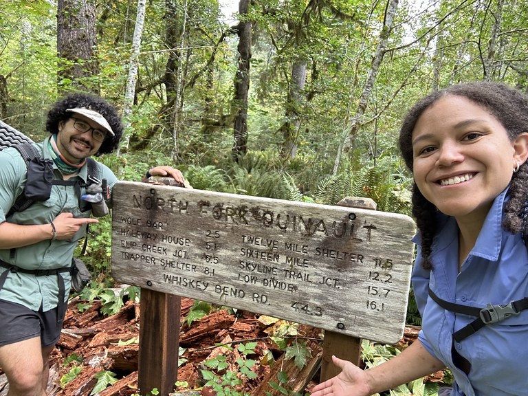 Two hikers take a selfie next to the North Fork Quinault trailhead sign.