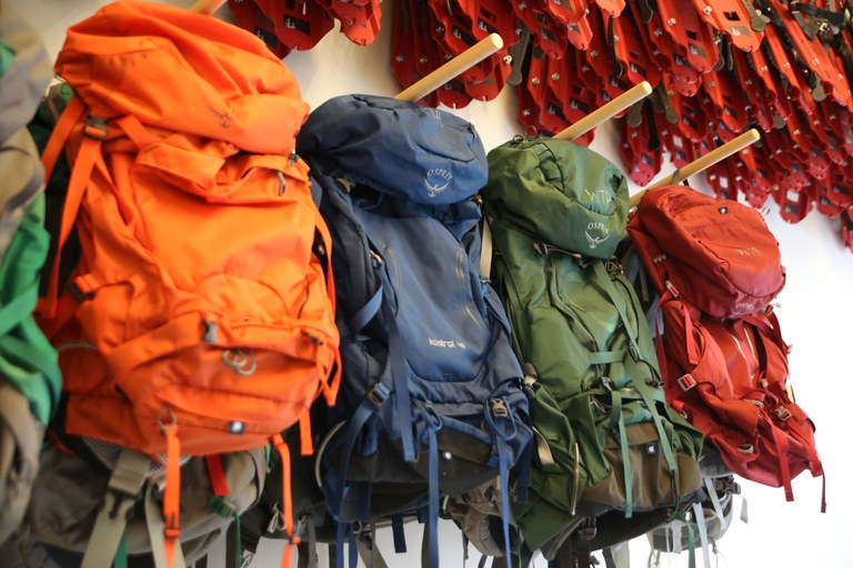 A few rows of WTA Gear Lending Library backpacks are organized on a wall.