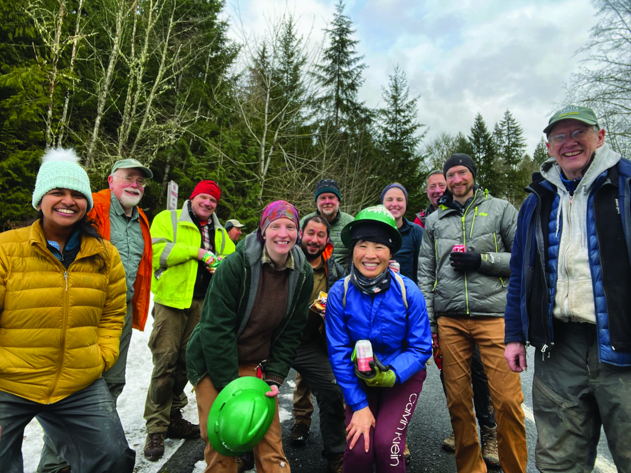 liza and crew Group of hikers smile at camera with trees and peaks of blue skies in the background.