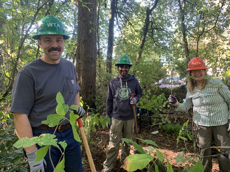 Three WTA volunteers with hard hats pose among foliage.