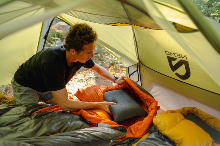 A hiker organizes his pillow and sleeping bag from within a tent.