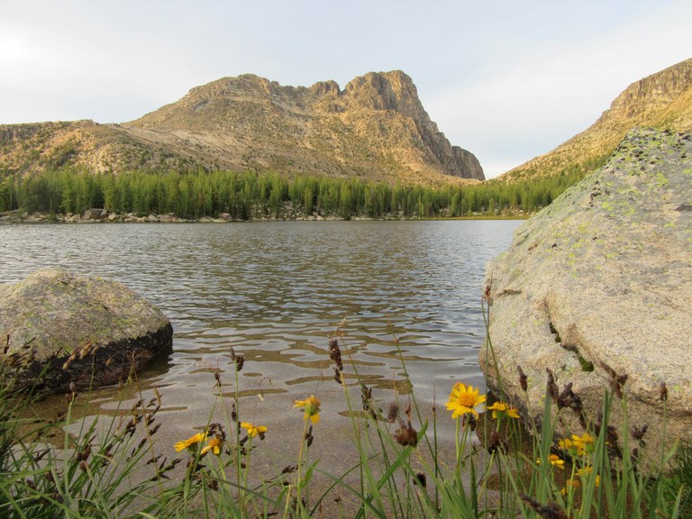 Rocky mountain rises behind a still lake in late afternoon light.