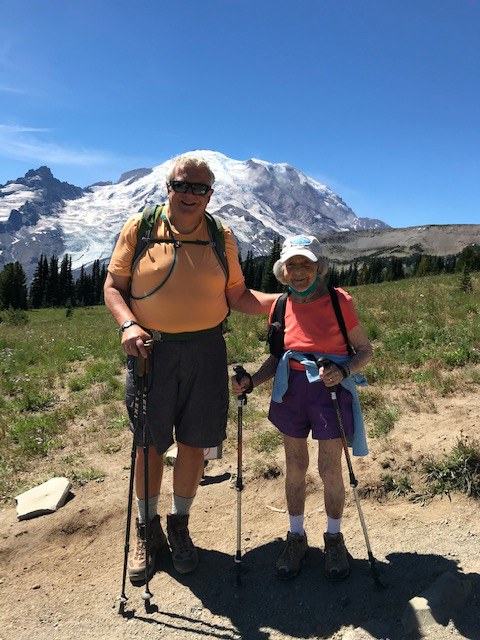 Bronka visiting Burroughs Mountain this past summer. Bronka and Bill stand on trail smiling at the camera, Mount Rainier behind them.