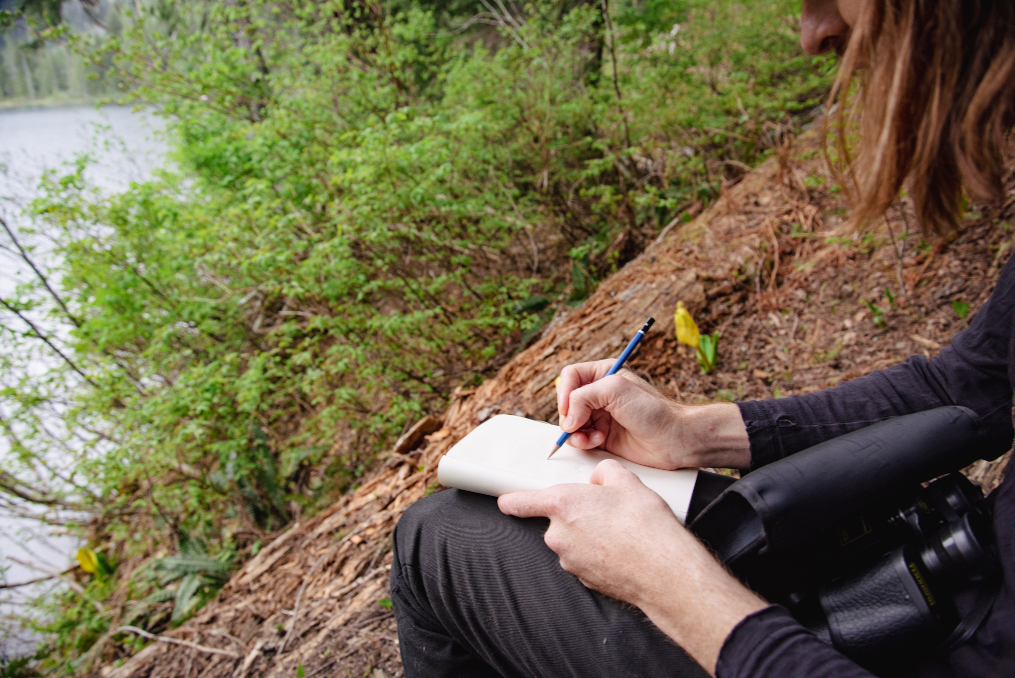 A close up of a hiker on trail sitting down to write in a notebook.