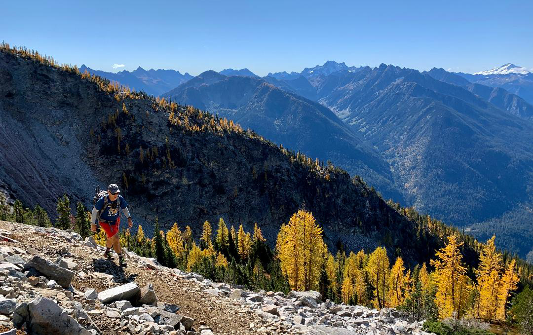 Craig hiking along a hillside with a valley of larches below.