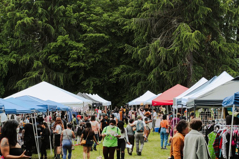 A dozen pop-up tents line a grass walk way, occupied by festival goers.