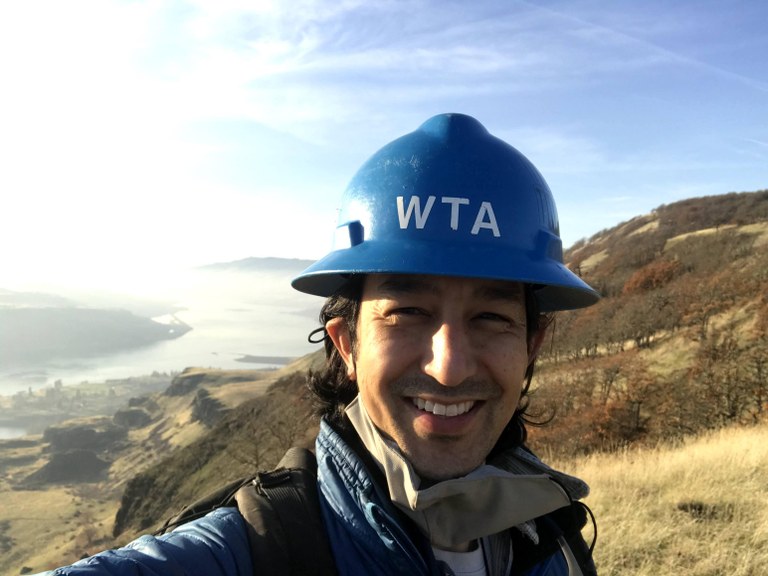 Ryan taking a selfie on trail while wearing his blue hard hat.