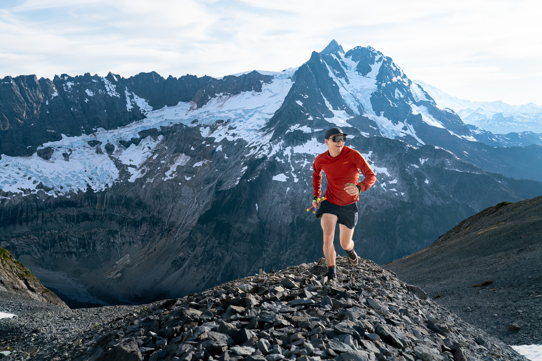 Person in red tshirt runs on top of gravel trail with beautiful mountain peaks in the background.