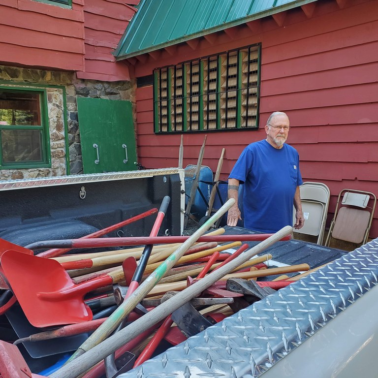 Pickup truck bed fully of tools and shovels with red building in background.