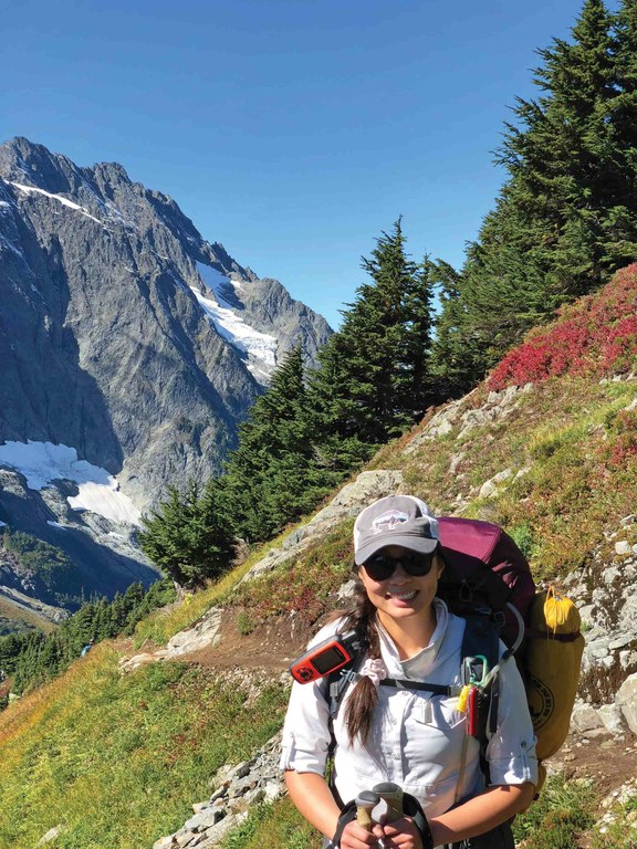 Whitney smiling at the camera in backpacking gear on the trail. Photo by Whitney Allar.