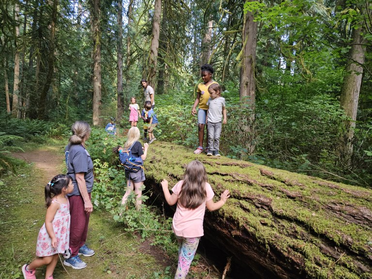 A hiking group with kids play on trail and on a log.