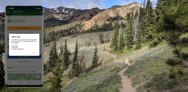 Hike details and the last few trip reports are a few of the features hikers can access offline with Trailblazer. A cellphone with the Trailblazer mobile app pulled up is displayed over a trailscape.