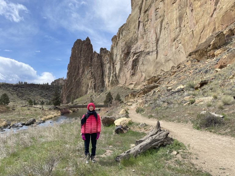 Smith Rock A hiker stands next to a trail in a desert canyon.
