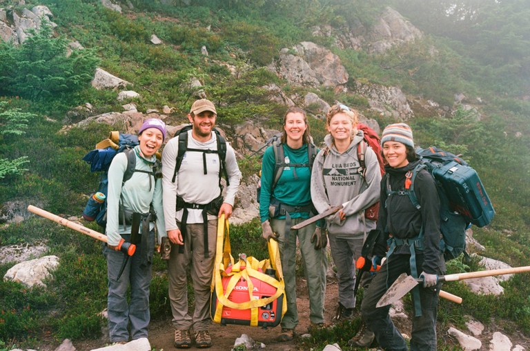 LTF crew members stand with backpacks and tools in their hands on a foggy day.