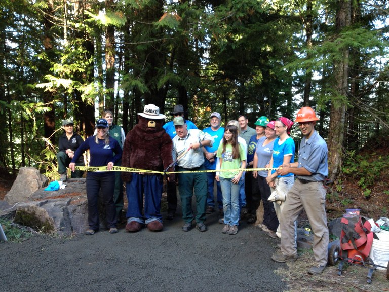A group stands behind the ribbon at the ribbon cutting/opening of the Volcano View Trail in Mount St. Helens National Monument in 2014. Photo from WTA Archives.