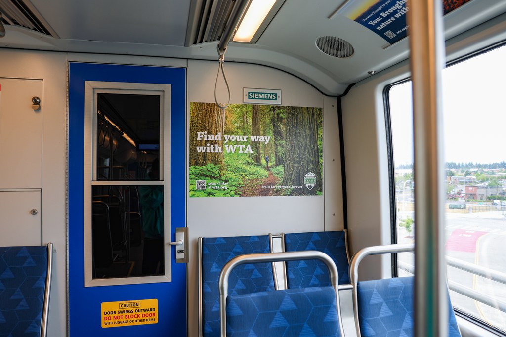 WTA ad on Sound Transit. WTA advertisement on Link Light Rail. Image of a hiker in a lush forest along with text "Find your way with WTA."