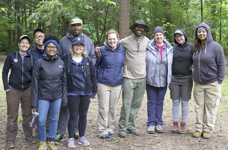 Becca Atkins A group of adults stand together smiling for the camera. Becca Atkins is third from right, wearing a warm hat and a raincoat.
