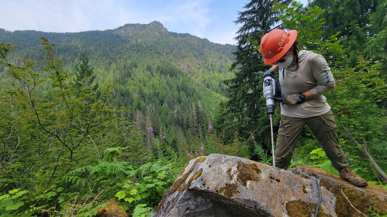 A WTA crew member drills through a rock with a rock drill.