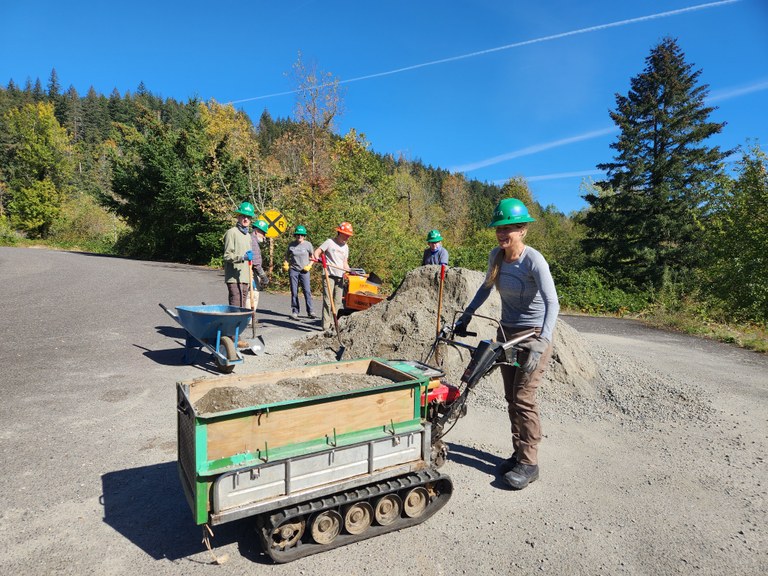 A woman operates a mechanized toter to move gravel from a large gravel pile in the background. 