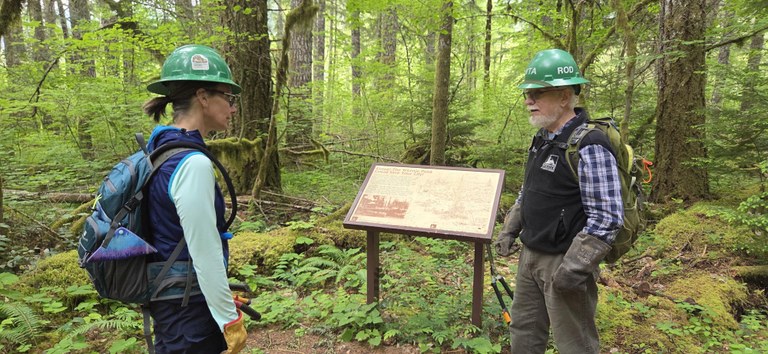 Two volunteers chat on trail wearing hard hats.
