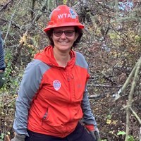 Women in orange hat and jacket smiles at camera.