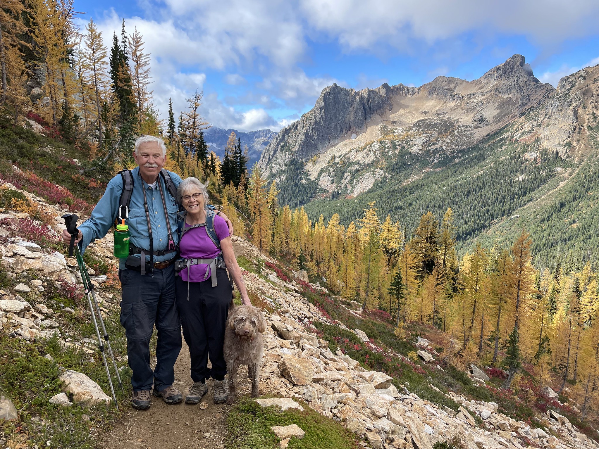 Photo by David Johnson Couple standing on hiking trail in front of larch trees and mountains