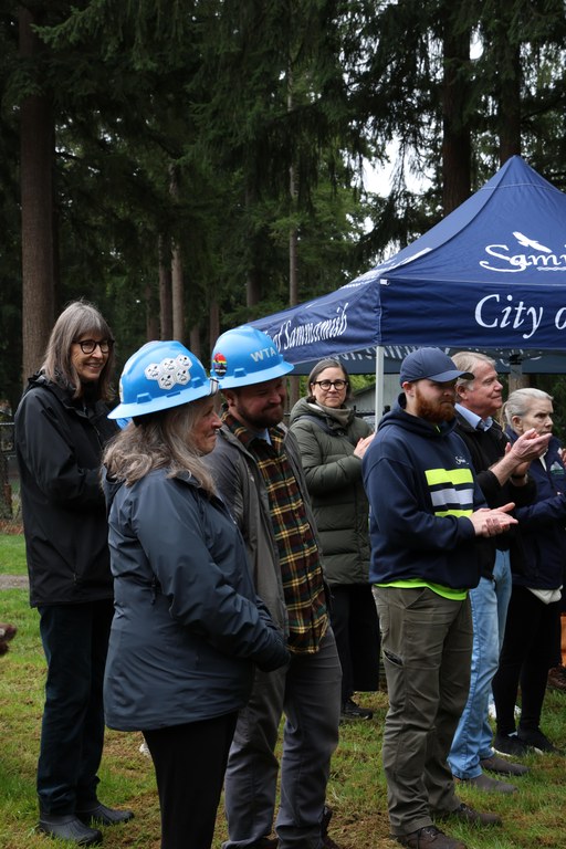 Two people in blue hard hats smiling while individuals around them clap for them.
