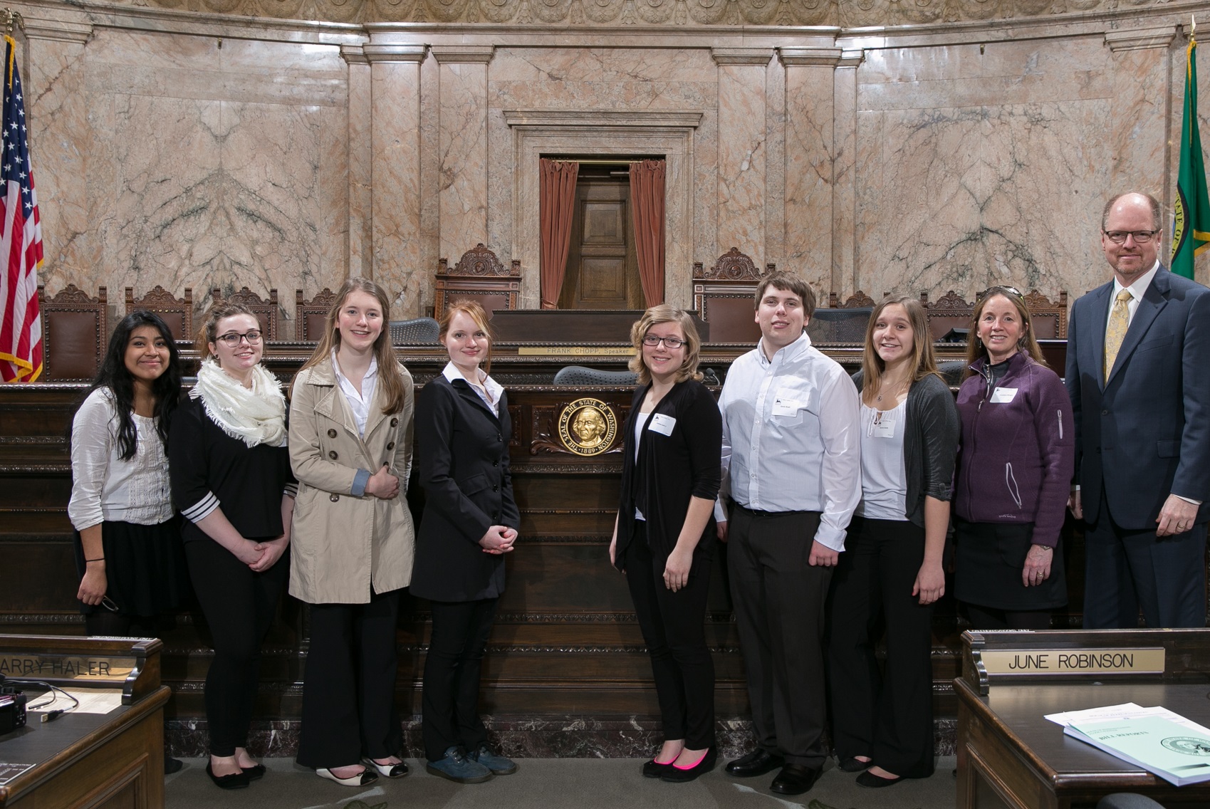 From left to right: Students Pabla Ventura, Nicole Cashman, Mckenzie Meyer, Tessa Thom, Emma Loney, Devin Boyd, Aurora Smith and club advisor Jackie Woolman-Morgan meet with Representative Dan Kristiansen in the House chambers.