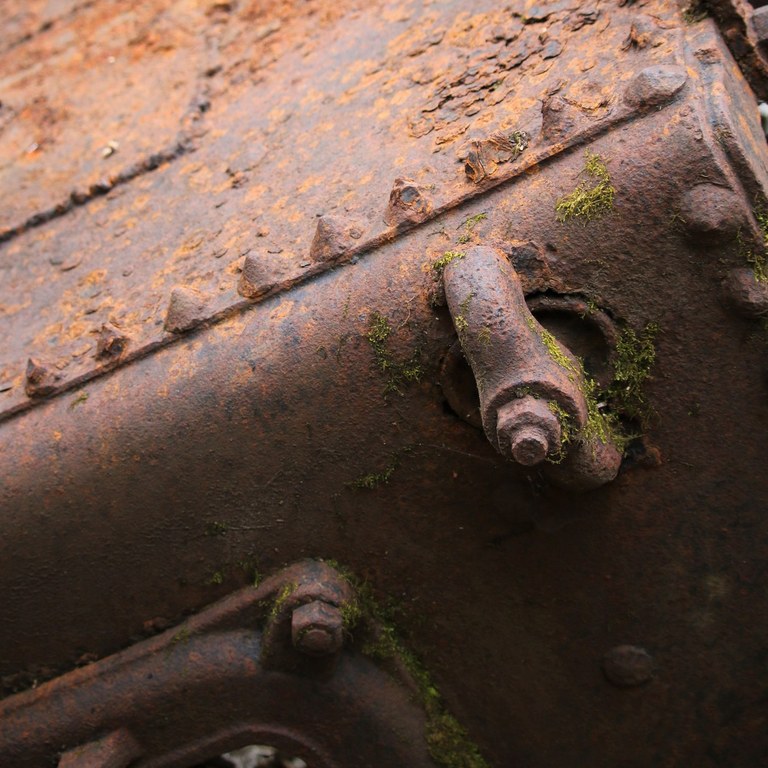 A rusted metal hull with fittings has moss growing on it.