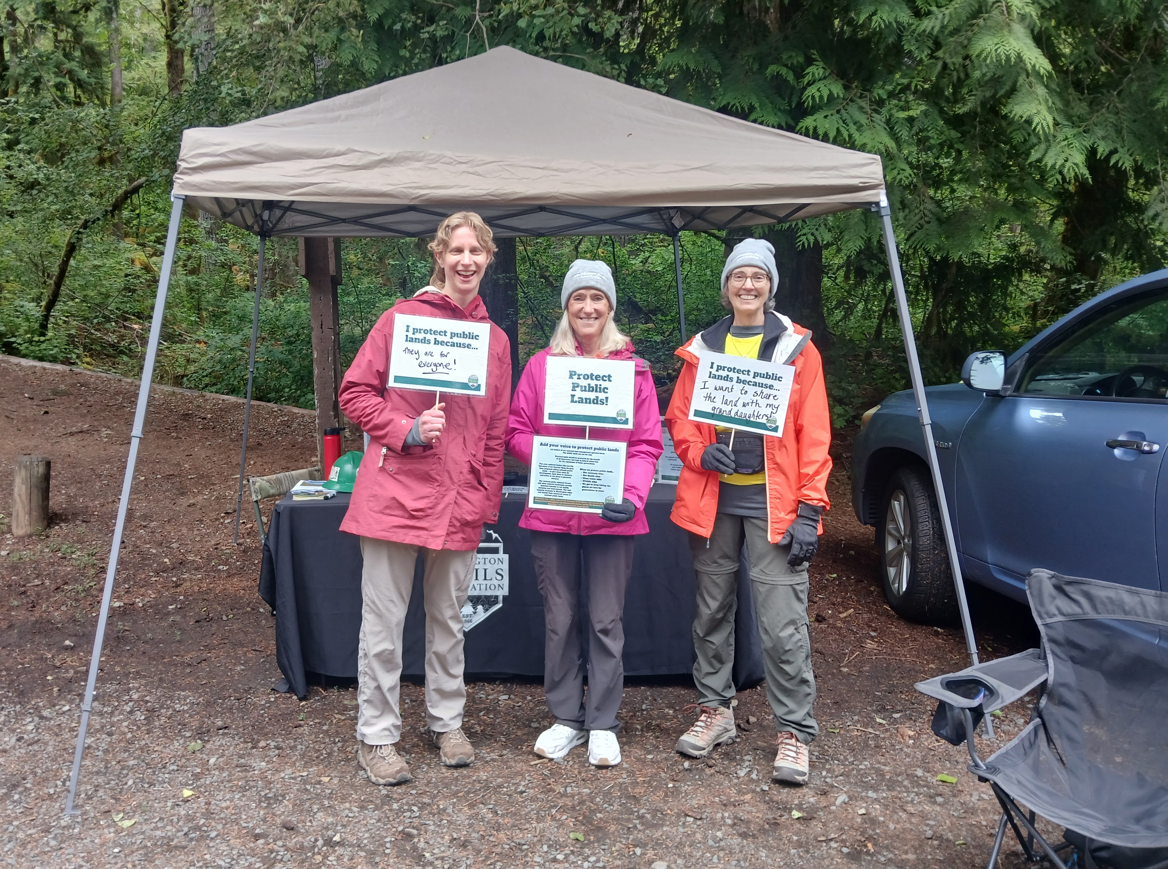 Three smiling people stand under a tent with a trail behind them