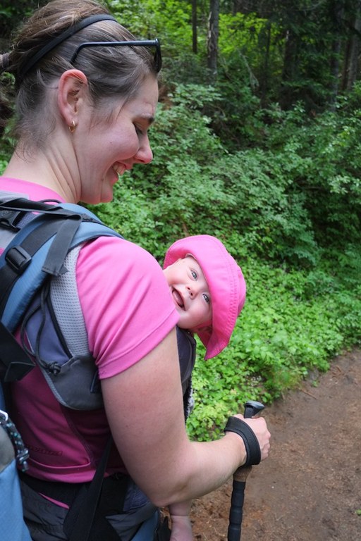 A parent wearing a large backpackg smiles down at a baby in a front carrier.