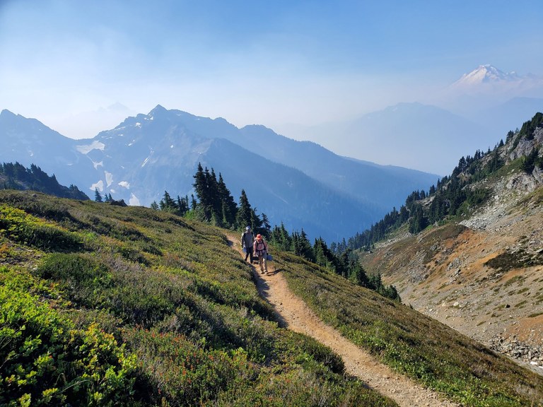 Backcountry response team trail work party crew members hike along the trail with tools, with Mount Baker in the background, on the Twin Lakes trail. Photo by Mike Bellis.