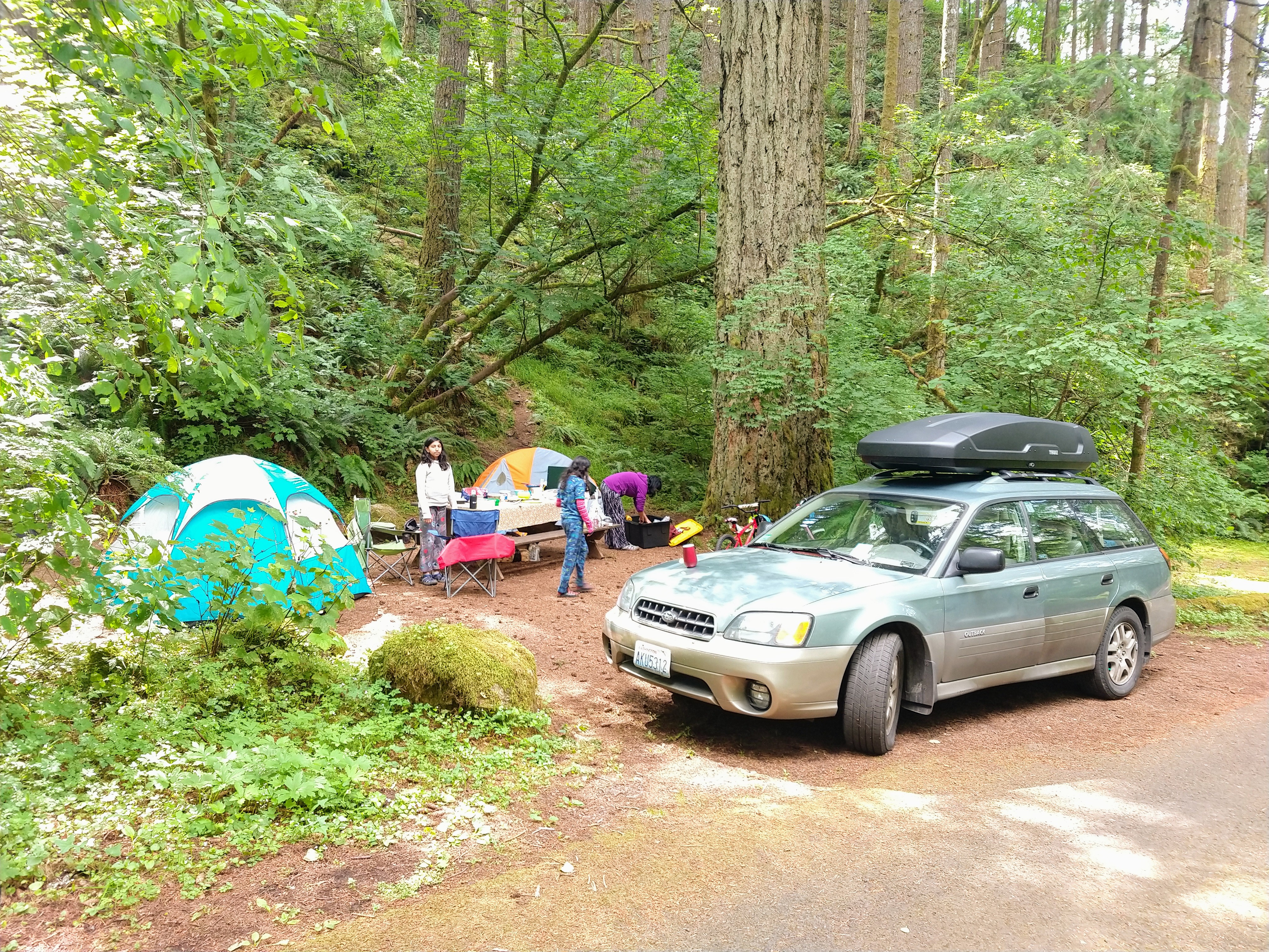 Family unpacking at a campsite with two tents and car parked in front
