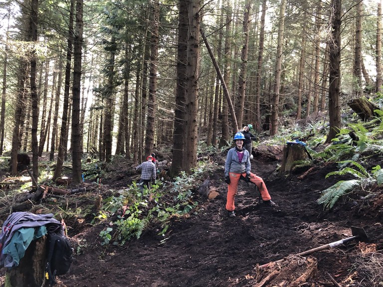 Becca stands in the middle of the planned route for the new trail. Photo by Martin Knowles Becca stands in the middle of the planned route for the trail. She smiles at the camera while volunteers work in the background.