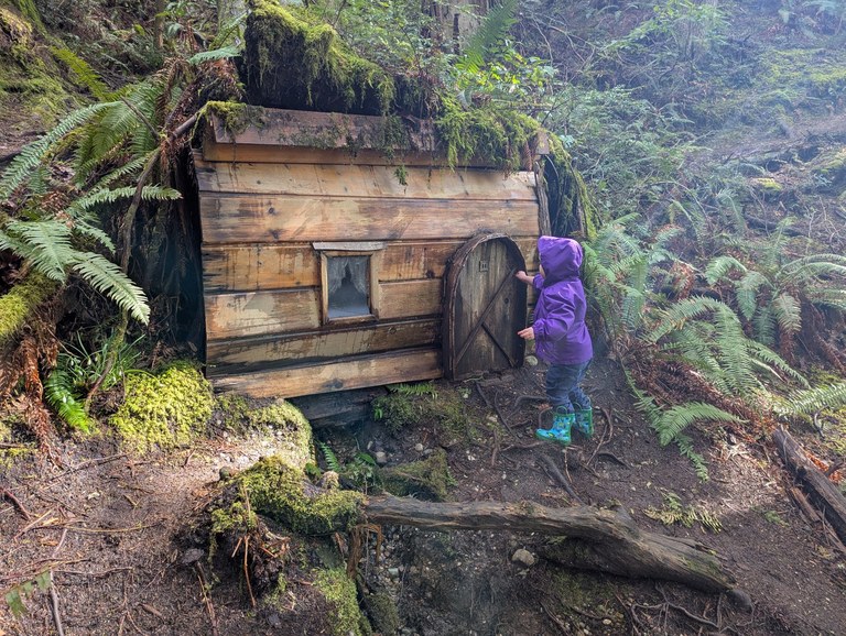 child in purple jacket explores small cabin on trail