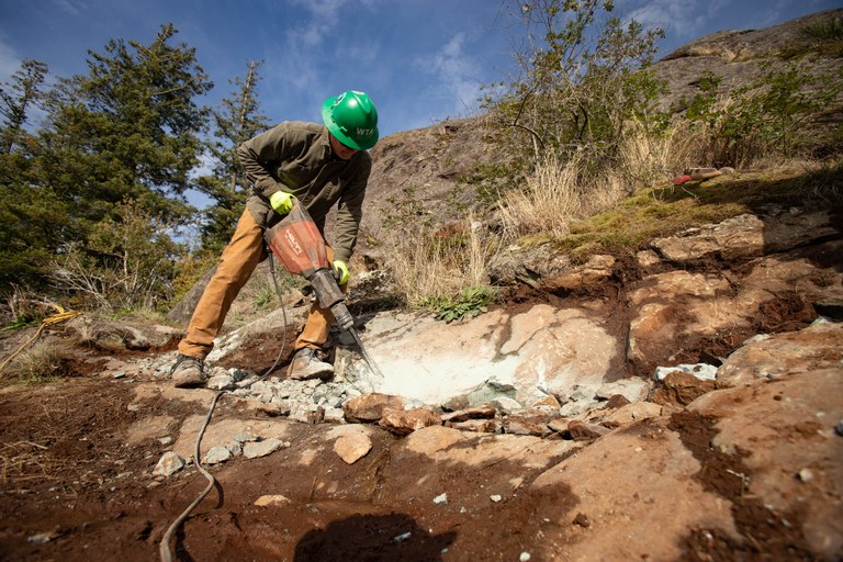 A WTA crew member uses a jackhammer on a section of rocky trail. 