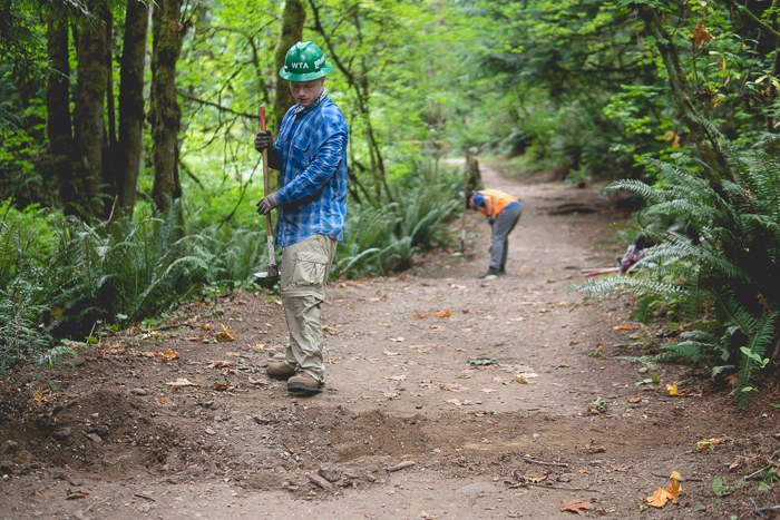 A volunteer hoes a swath of trail in the woods.