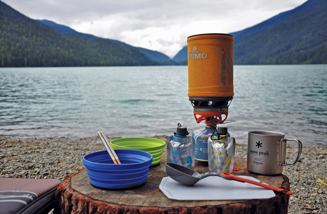 Camp stove. Camp stove with bowls and eating implements next to a lake.