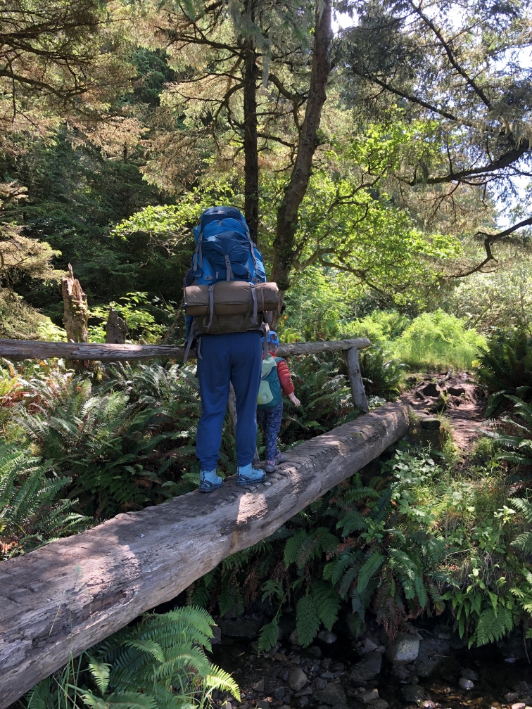 An adult with a backpacking pack and a young child cross a wooden bridge. Photo by Loren Drummond. 