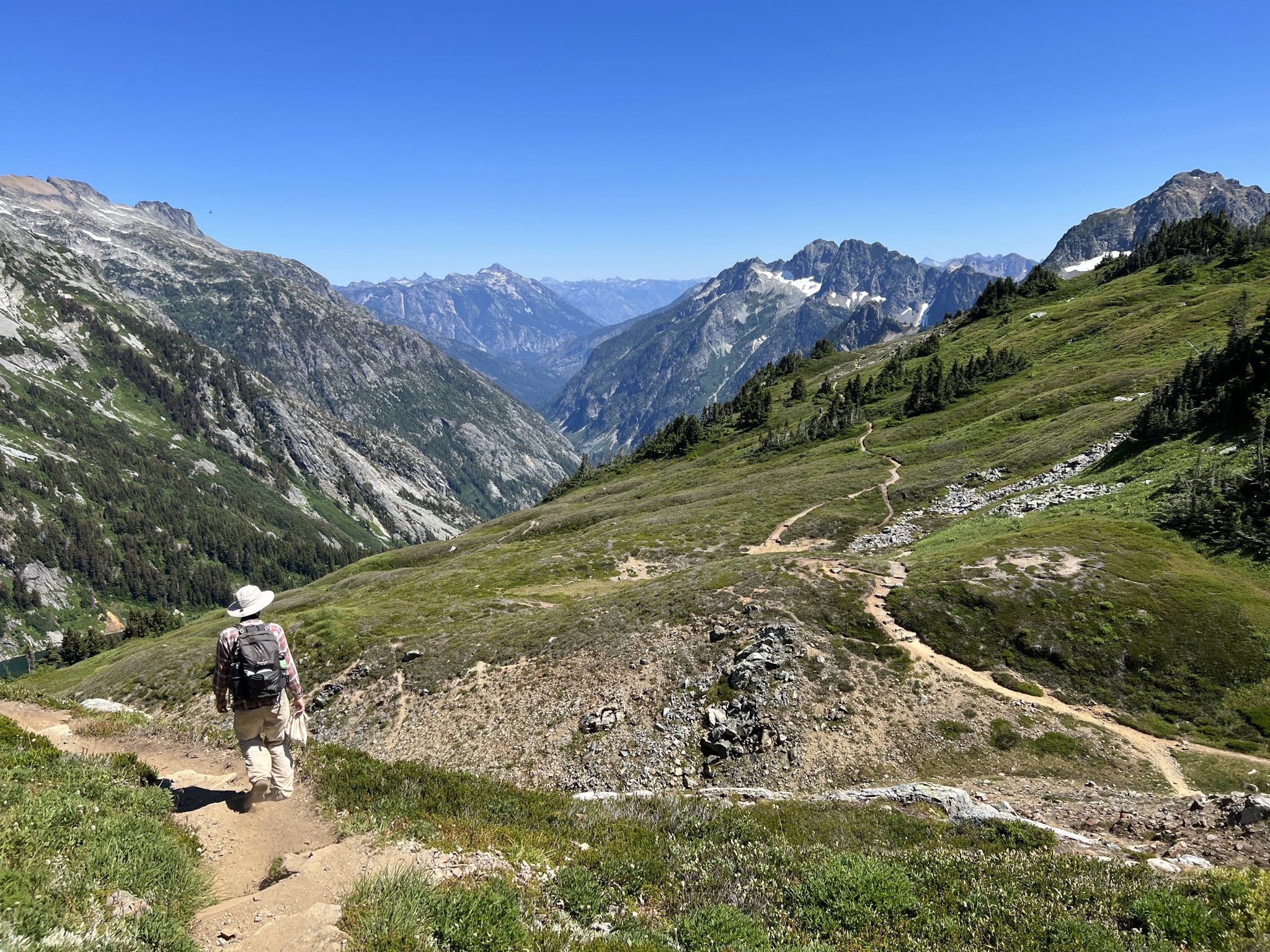 Hiker walks down a trail that winds through a valley with peaks as far as you can see