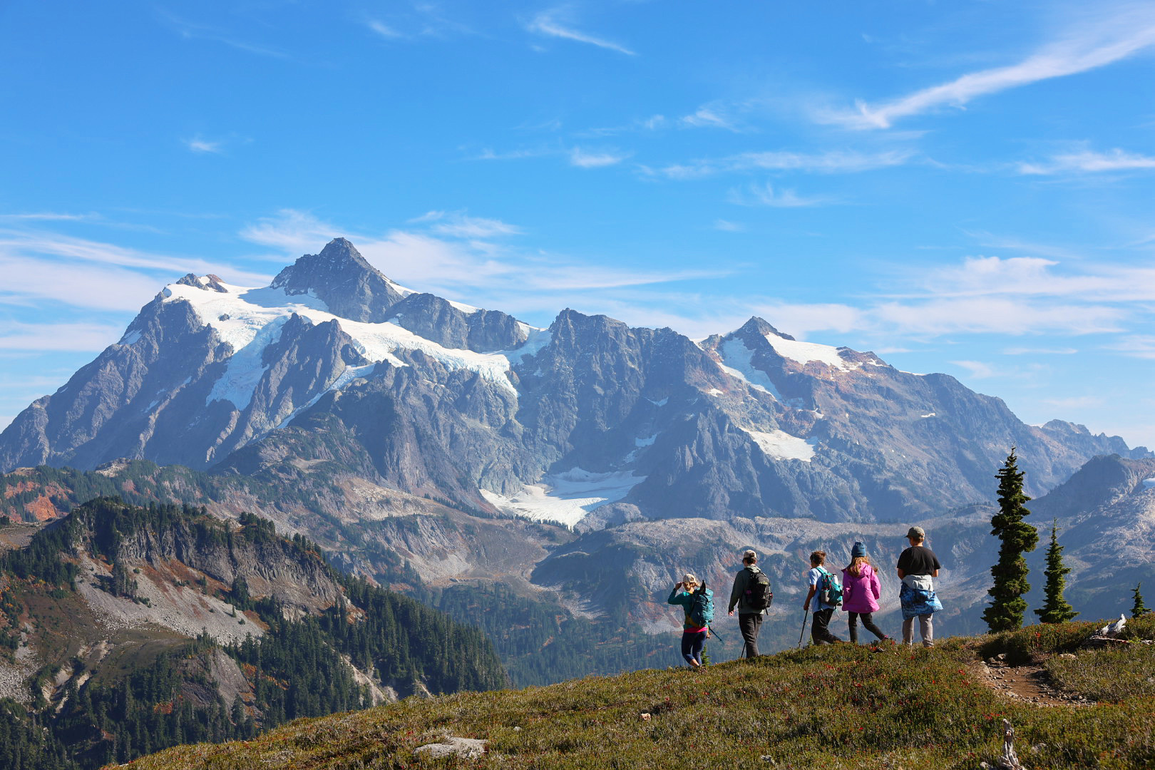 Five people stand on a ridgeline looking at jagged, snowy peaks