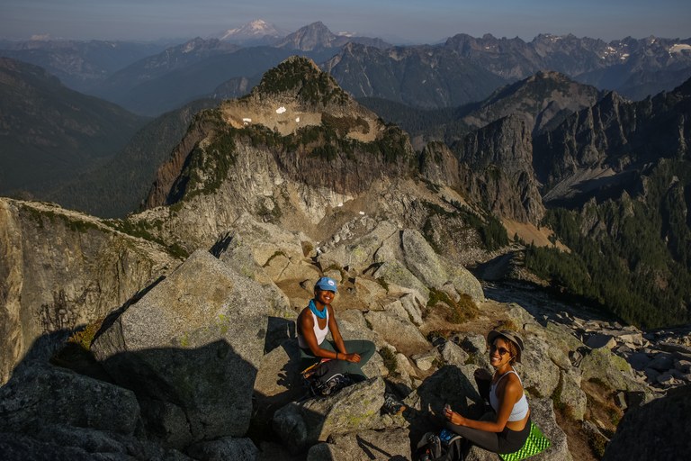 Project Reclamation Film. Two women of color sit on rocks, smiling up at the camera, with peaks reaching far into the distance.