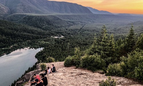 View from Rattlesnake Ledge at sunset. Several people are sitting on the ledge looking out over the ledge. 
