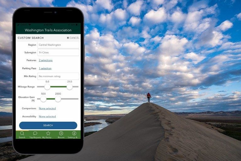 View of WTA Trailblazer app over photo of hiker walking on dune ridge. Philip Cho